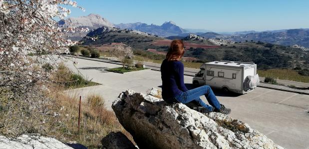 vrouw bij een bloesemboom bekijkt een camper in een berglandscha