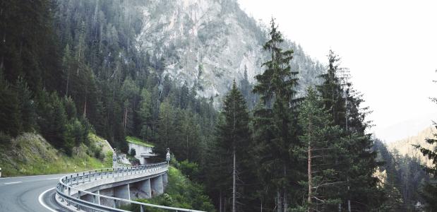 Photo by M. R. on Unsplash een slingerende bergweg tussen naaldbomen in Zwitserland